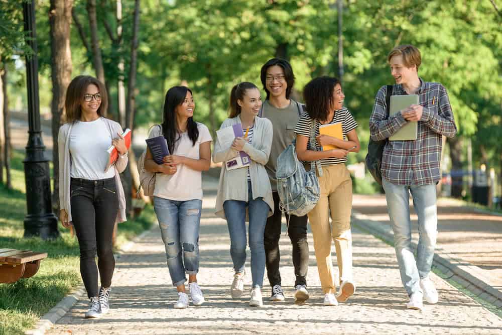 Happy young students walking outdoors Image of multiethnic group of happy young students walking outdoors. Looking aside.